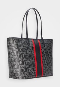 Taška přes rameno v černé a šedé barvě s opakujícím se vzorem loga, se svislými pruhy v červené a černé barvě. Vyrobena z texturovaného syntetického materiálu.