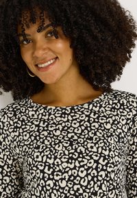 Top de leopardo en negro y beige con escote amplio y tejido suave, de corte holgado y mangas cortas.