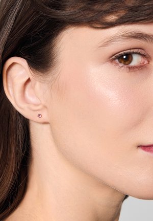 Mały różowy kamień szlachetny w kolczyku na sztyfcie, noszony na płatku ucha modelki, z polerowanym wykończeniem.