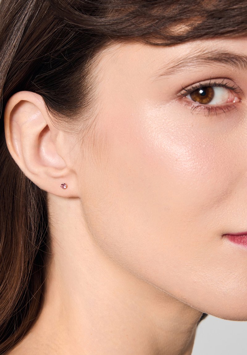 Mały różowy kamień szlachetny w kolczyku na sztyfcie, noszony na płatku ucha modelki, z polerowanym wykończeniem.