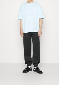 Světle modré tričko s krátkým rukávem s tie-dye vzorem, spárované s tmavými tapered kalhotami a černou obuví s bílými akcenty.
