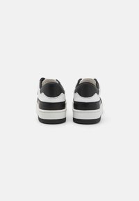 Sneaker bianco e nero con un tallone nero texturizzato, suola intermedia bianca liscia e colletto imbottito, caratterizzate da cuciture sottili nel design.