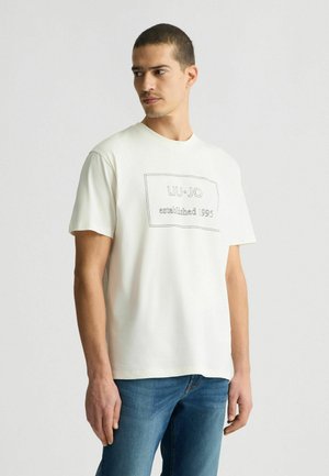T-shirt a maniche corte color crema realizzato in cotone. Presenta un logo rettangolare con "LIU·JO fondato nel 1995" in cucitura nera.