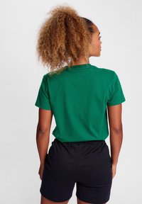 Camiseta de algodón verde con mangas cortas, cuello redondo y textura suave, combinada con pantalones cortos de cintura elástica negros.