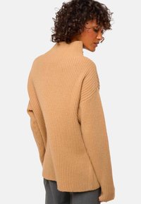 Beige Rippstrickpullover mit hohem Kragen und lockerer Passform. Strukturierter Stoff und überschnittene Schultern, mit einem leicht taillierten Saum.