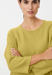 Limoengroen gebreide trui met een ronde hals, verlaagde schouders en geribbelde manchetten. De stof heeft een zachte textuur met lichte schaduwwerking.