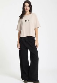 Cream cropped t-shirt with black graphic detail, paired with wide-leg black jeans. Fabric appears soft, with a relaxed fit and smooth texture.