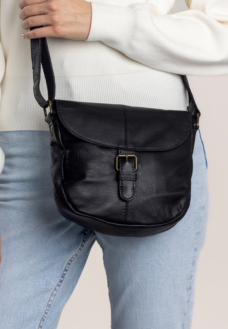 Svart läder crossbody-väska med rundad form, klaffstängning och subtila spänndetaljer. Justerbar rem och mjuk textur.