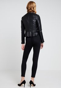 Giacca peplum nera in similpelle, con maniche lunghe, design aderente, dettagli delle cuciture verticali, abbinata a jeans skinny neri e tacchi.