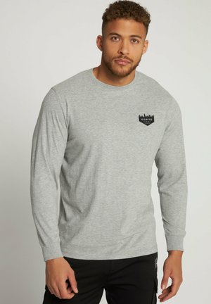 Grijze langslijf t-shirt in katoenmix met een ronde hals. Voorzien van een zwart logo op de linkerborst. Gladde textuur, normale pasvorm.