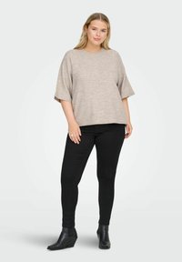 Top beige a maniche corte in maglia con vestibilità comoda, abbinato a jeans skinny neri e stivaletti alla caviglia. Texture liscia e design semplice.