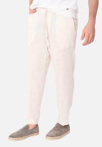 Pantaloni di lino beige chiaro con vestibilità ampia, fascia elastica in vita, coulisse e tasche laterali. Abbinati a scarpe slip-on in suede grigio.