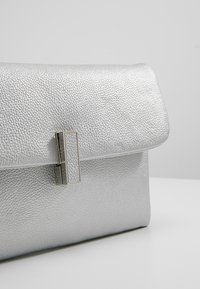 Silver metallic clutch bag with a textured surface, featuring a rectangular silver hardware clasp and a structured, fold-over design.