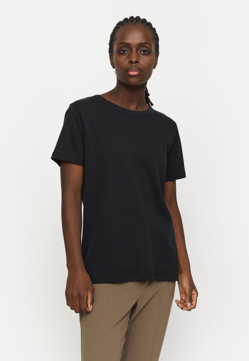 Black, short-sleeved t-shirt made of cotton with a round neckline and simple design. Worn with beige trousers.