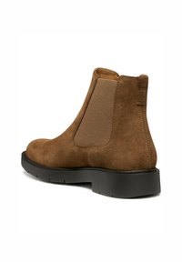 Bottines en daim marron avec des panneaux élastiques sur les côtés et une semelle en caoutchouc noir. Texture lisse avec des détails de couture sur le talon et les côtés.