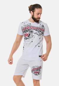 Witte katoenen t-shirt met zwart en rode grafische print, met een spetterontwerp. Gecombineerd met witte shorts met een vergelijkbare print.