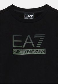 T-shirt nera in cotone con scollatura rotonda, caratterizzata da un grande logo EA7 e "EMPORIO ARMANI" stampato in contrasto sulla parte anteriore.