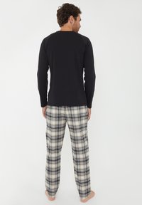 Chemise noire à manches longues associée à un pantalon de pyjama à carreaux en crème, noir et gris. Tissu doux avec une coupe décontractée et une taille élastique.