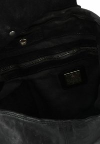 Interno di una borsa a tracolla in pelle nera con una texture liscia, tasca con zip, etichetta con logo e chiusura a scatto.