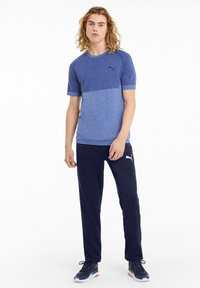 Blå atletisk T-shirt med tekstureret overdel, ensfarvet underdel, parret med ensfarvede marineblå bukser. Begge har Puma-logoet.