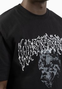 Czarny bawełniany t-shirt z grafiką wilka i zniekształconym napisem "Wasted Paris" w białym kolorze, okrągły dekolt, krótkie rękawy oraz miękka tekstura.