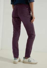 Pantalons slim violets avec une texture subtile, poches arrière et taille mi-haute, associés à des baskets blanches avec des accents bleus.