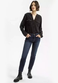 Czarna koszula z guzikami i dwiema kieszeniami na piersi, zestawiona z ciemnoniebieskimi dżinsami. Model nosi czarne botki za kostkę z masywną podeszwą.