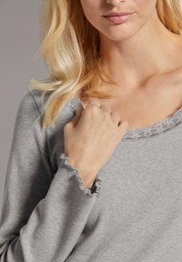 Lichtgrijs langemouwen top met een geribbeld textuur, geschulpte kantafwerking bij de halslijn en gefruitte mouwen, die een ontspannen pasvorm benadrukt.