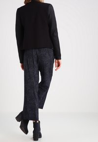 Czarna marynarka z teksturowanymi rękawami, zestawiona z luźnymi, ciemnymi spodniami w wzory oraz czarnymi botkami za kostkę. Czyste linie i nowoczesna sylwetka.