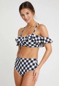 Biquíni aos quadrados em preto e branco, com um top froufrado e alças fora do ombro, e calções de cintura alta com padrão semelhante.