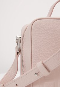 Borsa a mano in pelle rosa con superficie texture, dotata di una cerniera e di una tracolla in argento. Forma rettangolare compatta con linee pulite e minimi dettagli.