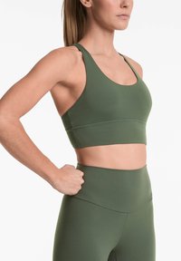 Zelena športna modrček iz gladkega, raztegljivega blaga z širokim pasom in izrezom v obliki žlice, v kombinaciji z usklajenimi visokimi leginami.