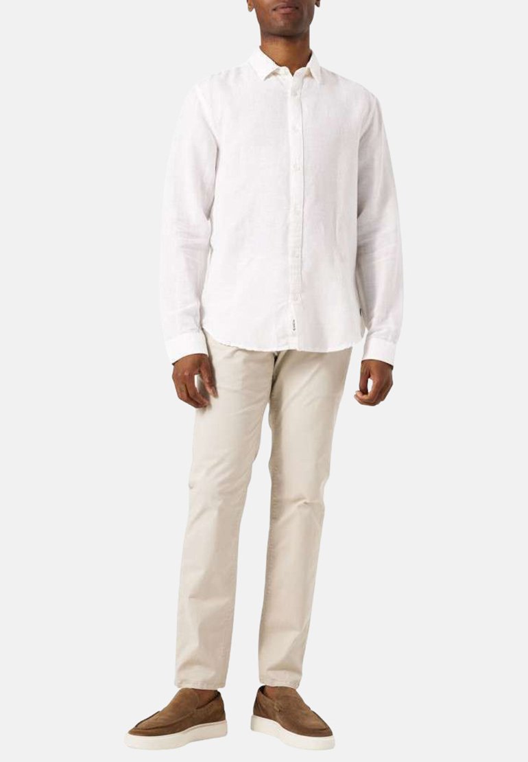 Witte linnen blouse met lange mouwen en knopen aan de voorkant, gecombineerd met beige broek en bruine instappers, staand tegen een neutrale achtergrond.