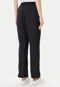 Pantaloni sportivi neri, larghi e con vita elastica, tasche laterali e un tessuto morbido e leggero. Indossati con sneakers bianche.