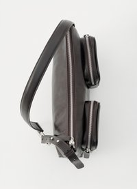 Tmavě hnědá kožená kabelka přes rameno s nastavitelným popruhem a třemi stříbrnými zipovými přihrádkami na jednobarevném bílém pozadí.