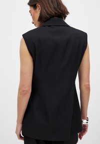 Must lähketuseta bleiser musta värviga, millel on struktureeritud õlad, sile kangas ja kohandatud sobivus, millel on nurgakrae ja tagaõmbluse detail.