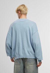 Világoskék, oversized kötött pulóver, kerek nyakkivágással és laza szabással. Vastag bordázott mandzsetták és derék. 