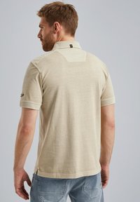 Polo beige à manches courtes avec col, en tissu texturé, un motif subtil sur le dos, et de petites fentes sur les côtés à l'ourlet.