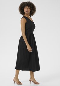 Svart midiklänning med figursydd bodice och volangkjol. Har en axelrem och en slät, elastisk tygtextur.