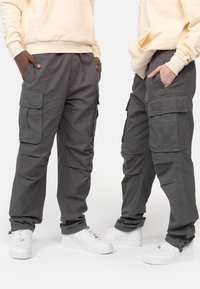 Gray cargo pants with multiple pockets, elastic cuffs, and a relaxed fit, paired with white sneakers and a light-colored hoodie.