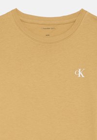 Beige tričko Calvin Klein Jeans s kulatým výstřihem, velikost 8 (128), s malým bílým logem "cK" na hrudi.