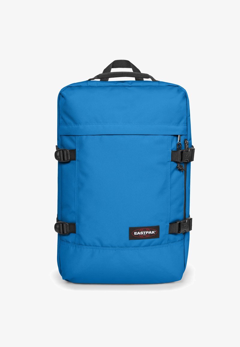 Sac à dos en tissu bleu de forme rectangulaire, équipé de boucles réglables, d'une poche zippée et d'un écusson logo dans le coin inférieur.