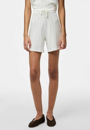 Combinaison blanche texturée avec une taille à cordon ajustable. Jambes courtes avec une coupe décontractée. Portée avec des chaussures plates en cuir marron.