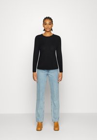 Top preto de manga longa com padrão canelado e decote redondo, combinado com jeans de perna reta azul claro e calçado de salto castanho.