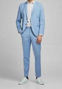 Ljusblå kostym med en skräddarsydd passform, med notch-lapel, två knappar och sidofickor, i kombination med en mönstrad skjorta och vita sneakers.