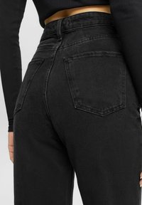Jeans de mezclilla negros de tiro alto con pierna recta. Presenta dos bolsillos traseros y detalles de costura sutiles. Tejido texturizado.