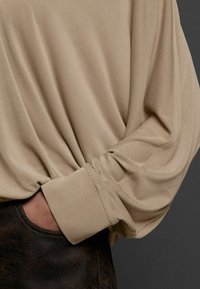 Beige pikad varrukad, pehmest kangast, laia lõikega, kergete keeratud mansettidega ja siledast tekstuurist, koos tumejoontega, struktuurseid pükse.
