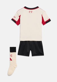Back view of a beige and red short-sleeve sports jersey, black shorts, and one beige sock with black cuff and red lettering.