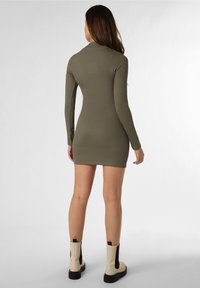 Vihreä oliivinvärinen ribbimekko pitkillä hihoilla, tiukka siluetti ja lyhyt helma. Yhdistetty kermaanvärisiin nilkkureihin, joissa on mustia yksityiskohtia.