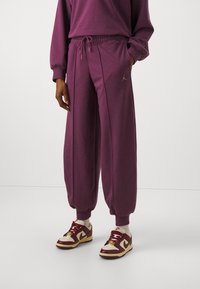 Liilat ylipitkät collegehousut, joissa kiristysnyöri vyötäröllä, kiiltävä hopeinen logo ja ribbineulotut resorit, yhdistetty viininpunaisiin ja kermaan vivahtaviin tennareihin.